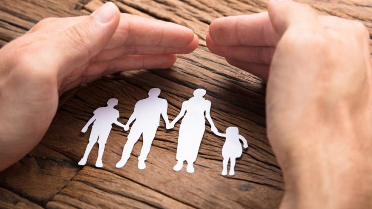 Photograph of hand protecting a paper cut-out of a family.